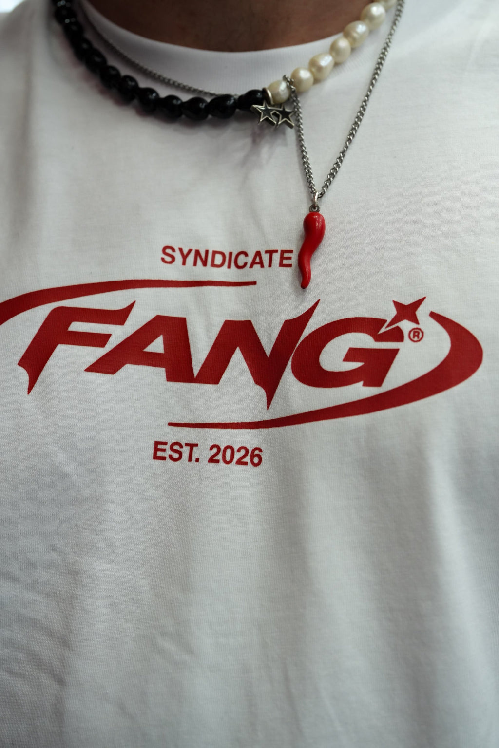 detalle de la camiseta sello en blanco, cuelgan dos collares, uno con un peperoncino napolitano.